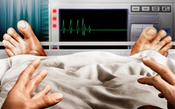 Frightened man in hospital bed seeing flatline pulse trace on monitor