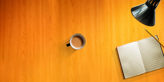 Overhead view of desk with cup of tea, pencil and blank note pad