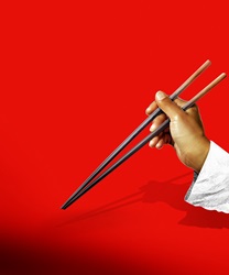 Hand holding chopsticks on red background