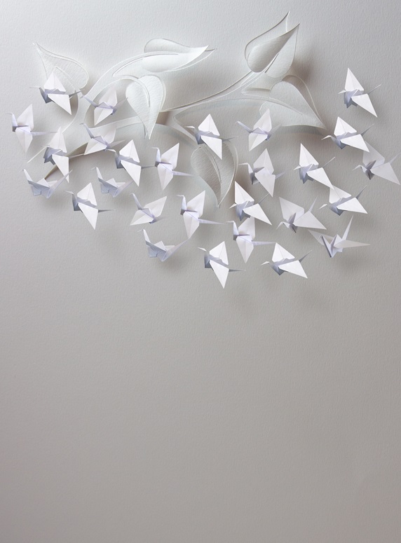 Origami paper cranes flying around twig with leaves